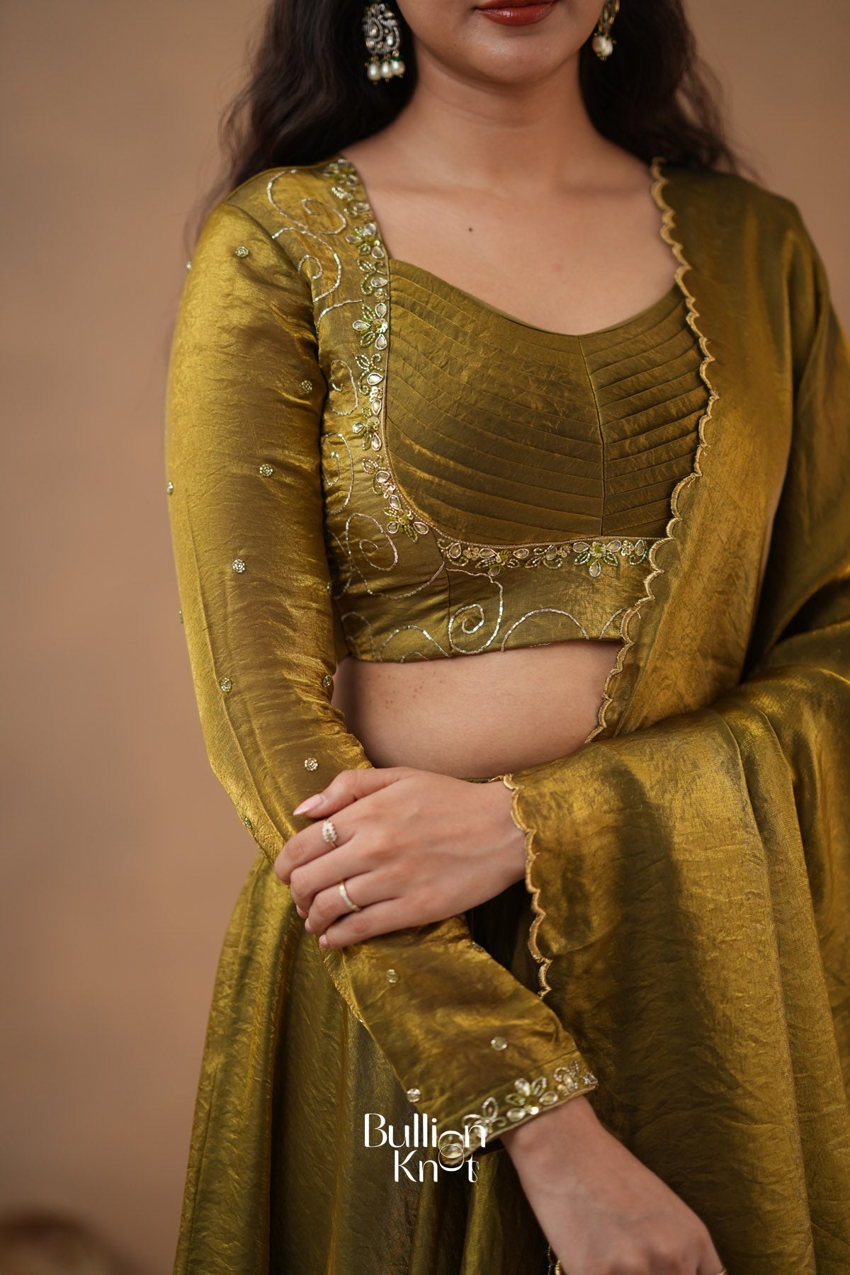 Woman wearing a green traditional outfit with gold embroidery on a brown background
