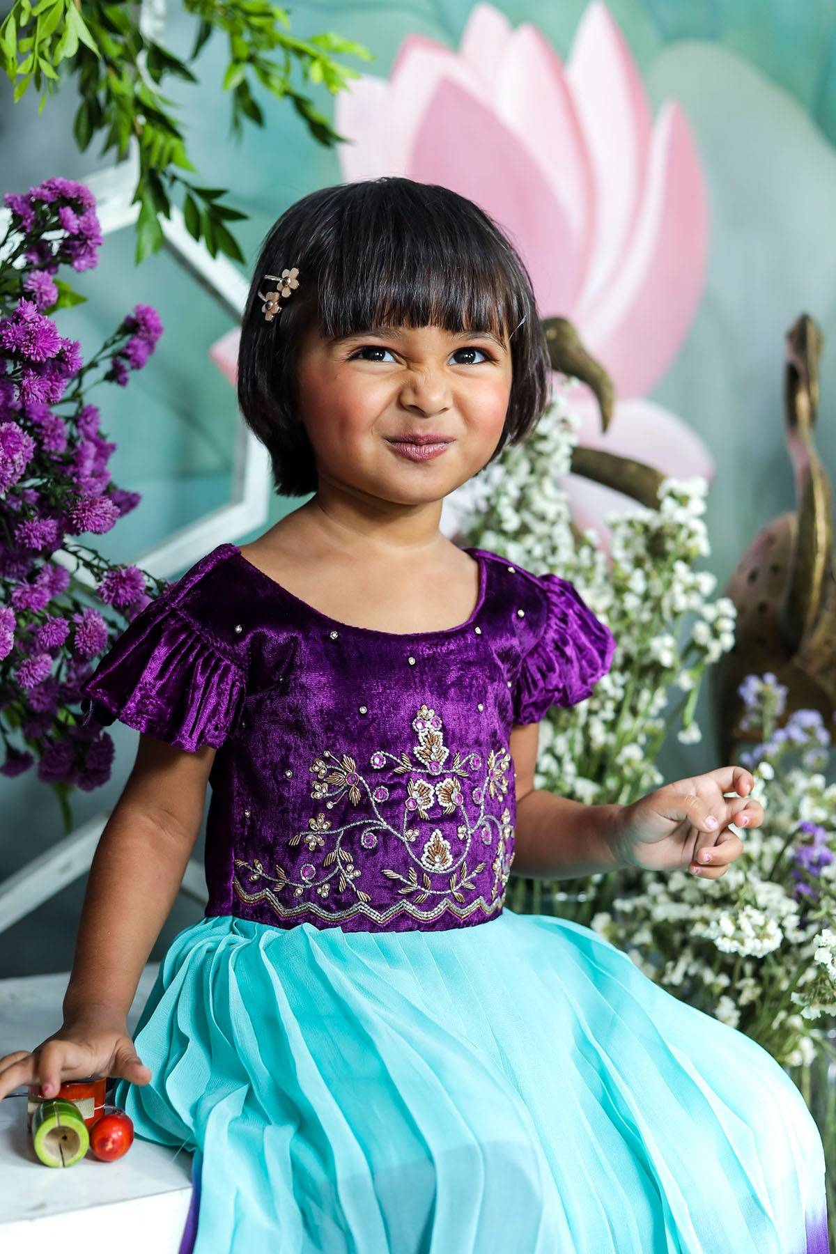 Child smiling in purple Baby Afsa Frock, floral decor