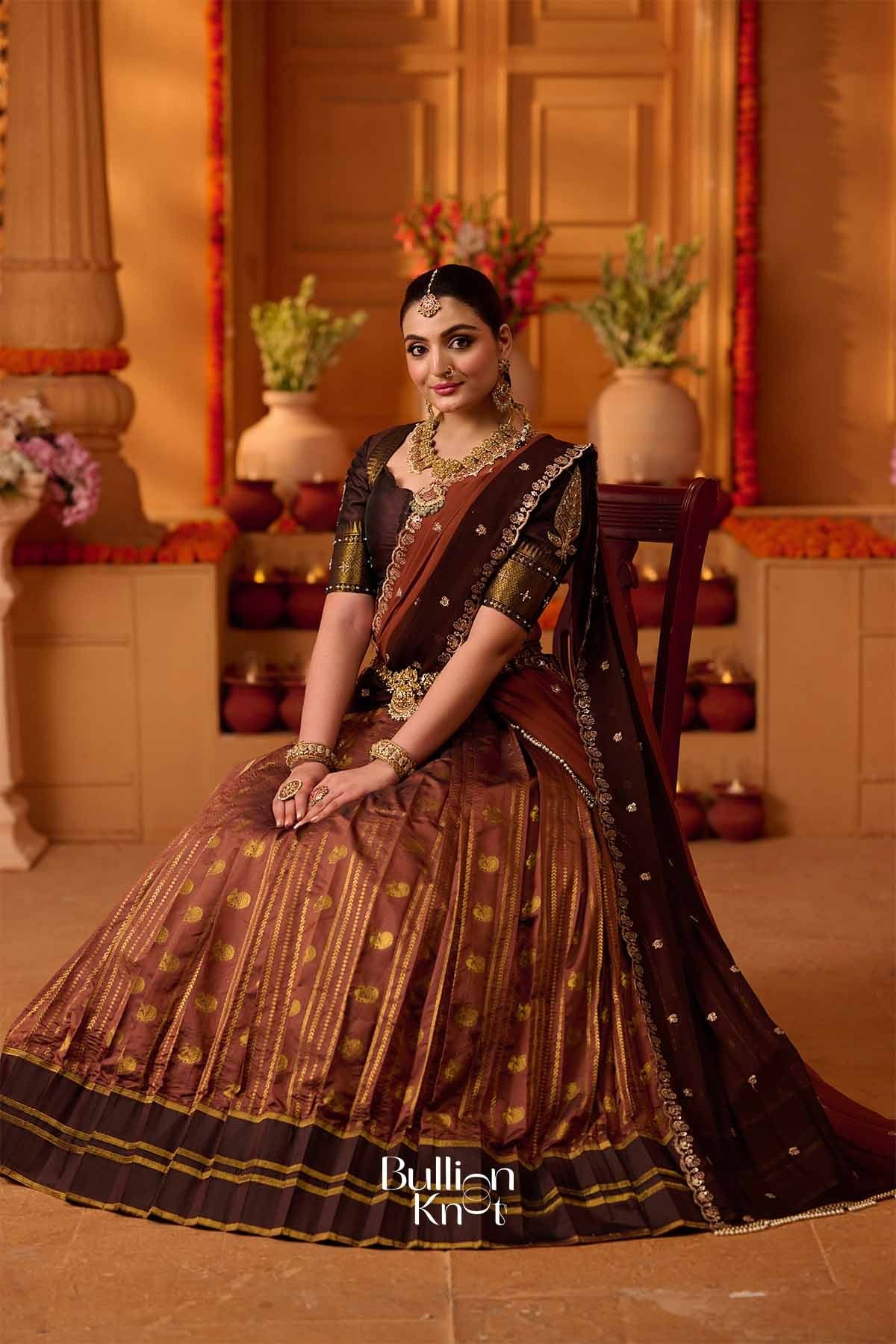 Traditional brown and gold lehenga set with pleated skirt, embroidered blouse, and matching dupatta, adorned with jewelry for festive celebrations