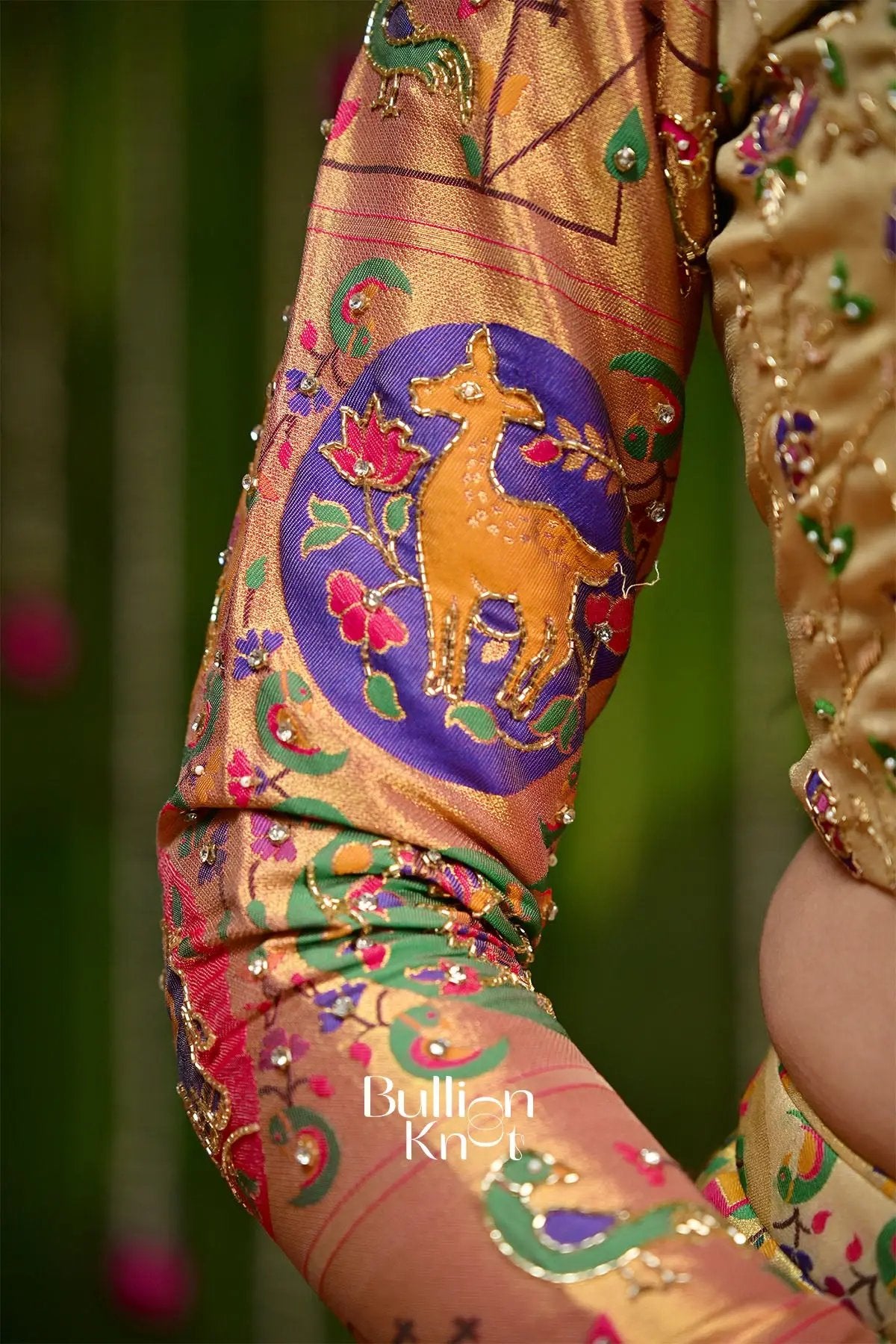 Close-up of embroidered gold and purple silk saree sleeve with deer motif
