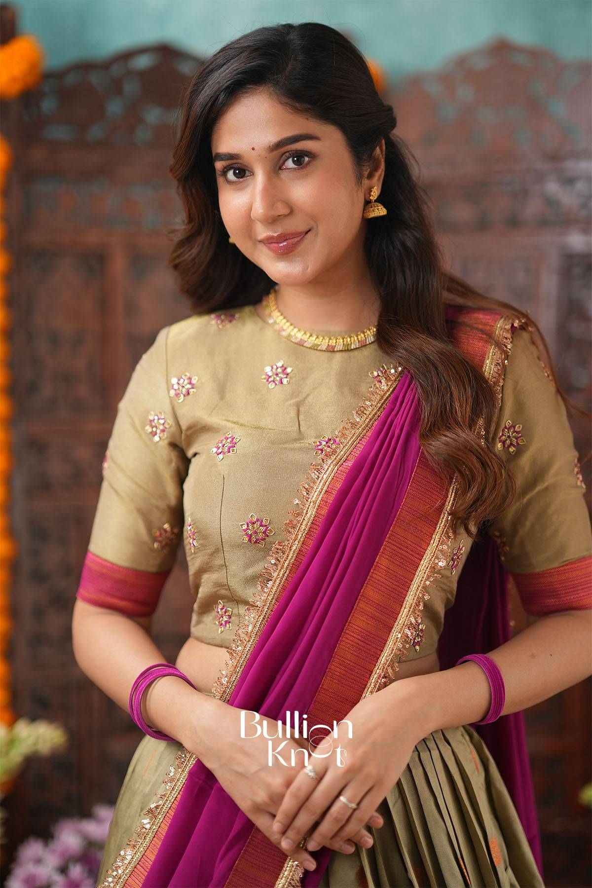 Close-up of woman in beige and magenta lehenga showcasing jewelry and detailed embroidery