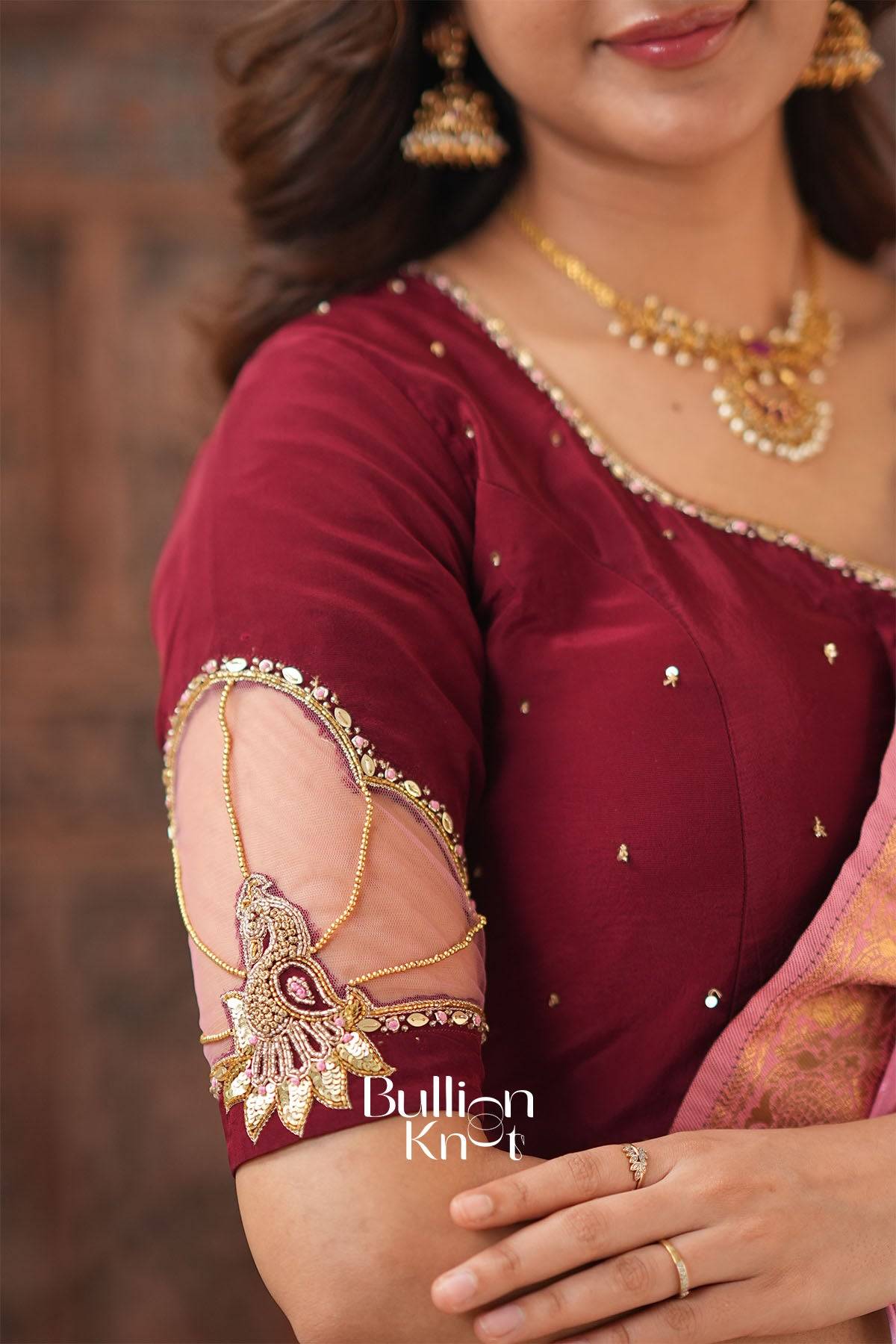Close-up of woman wearing maroon blouse with intricate embroidery and traditional jewelry, showcasing festive attire details