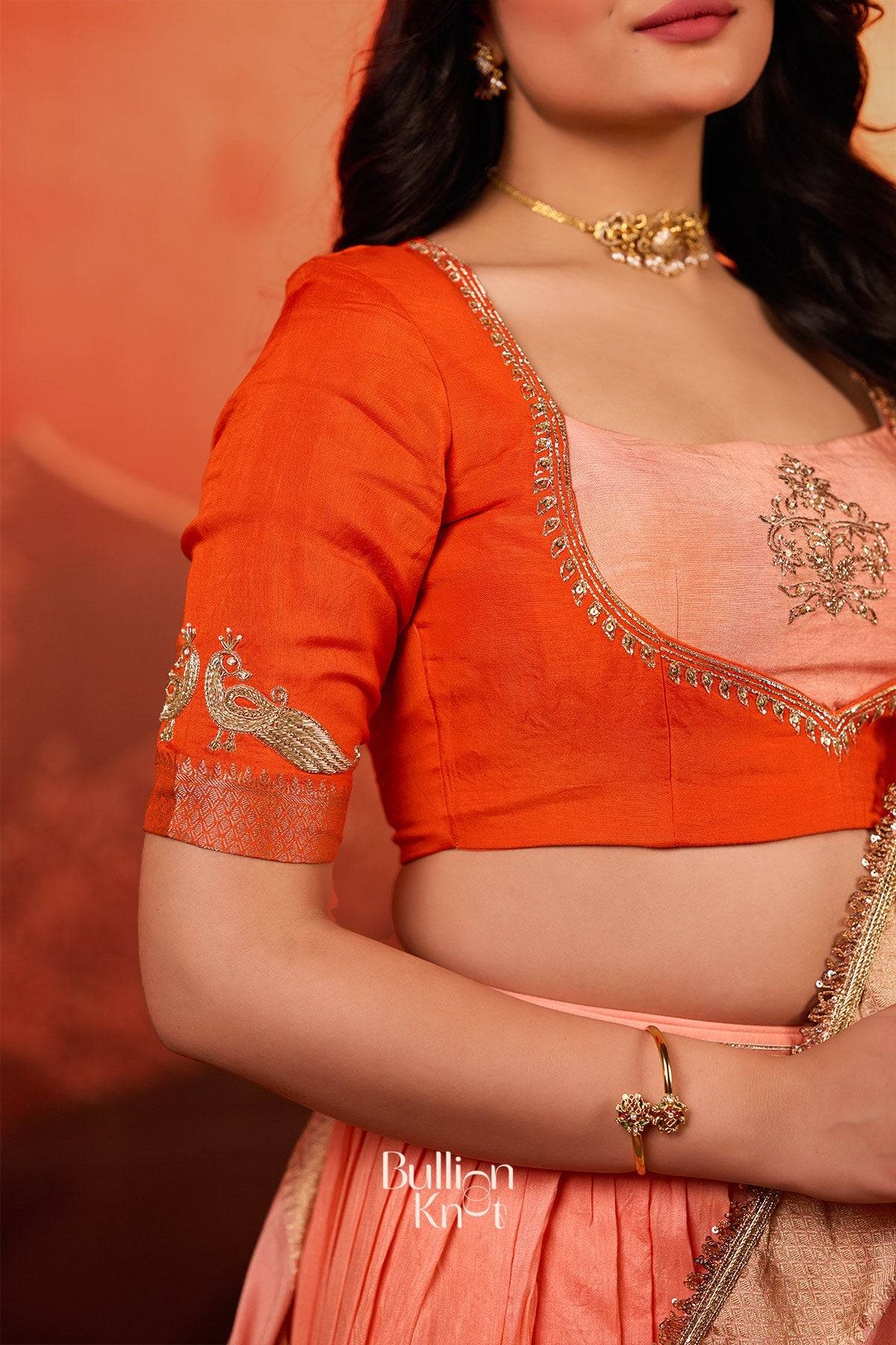 Detailed view of blouse embroidery from the Kaavya Dola Lehenga Set in Orange at bullionknot, showcasing intricate zari and peacock motifs.