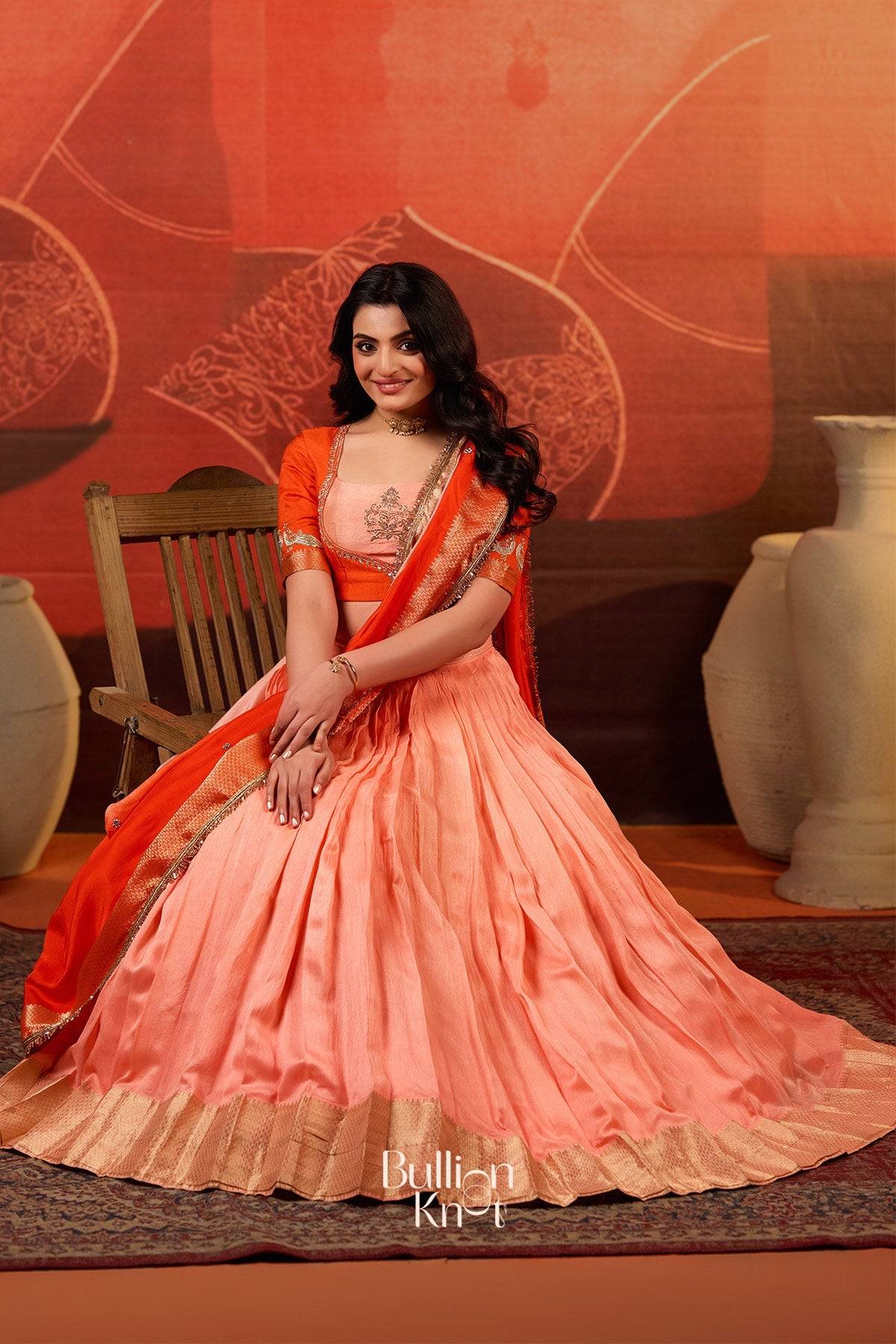Seated model in Kaavya Dola Lehenga Set in Orange at bullionknot, highlighting the graceful fall and sheen of the silk lehenga.