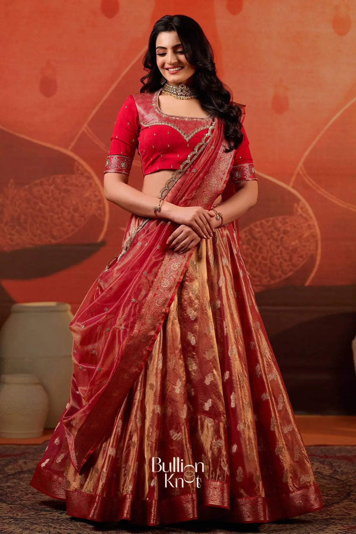 Elegant pose in Exclusive Lehenga - Amulya Tissue Zari Lehenga Set in Red at bullionknot, highlighting the luxurious zari woven lehenga and dupatta.