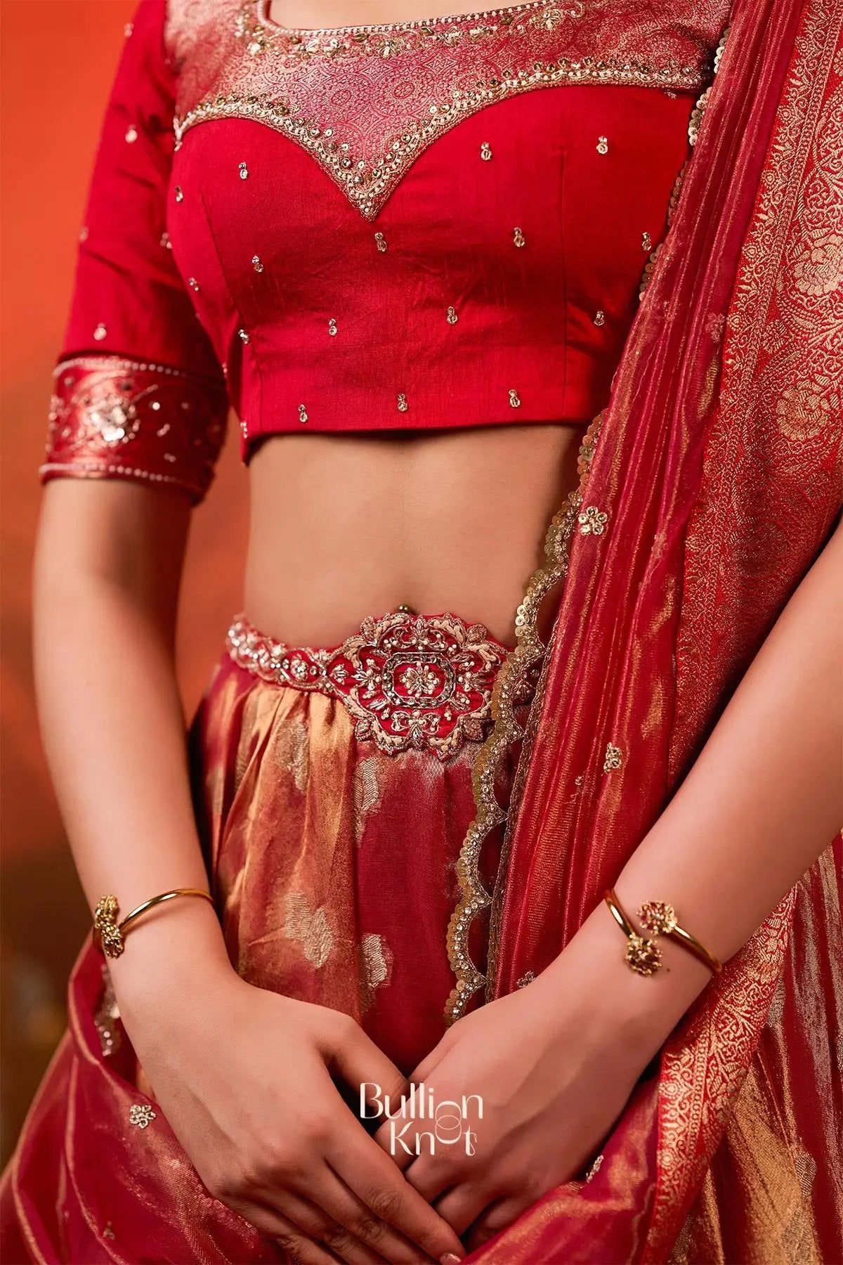Detailed close-up of Exclusive Lehenga - Amulya Tissue Zari Lehenga Set in Red at bullionknot, focusing on the ornate waist belt and zari embroidery.