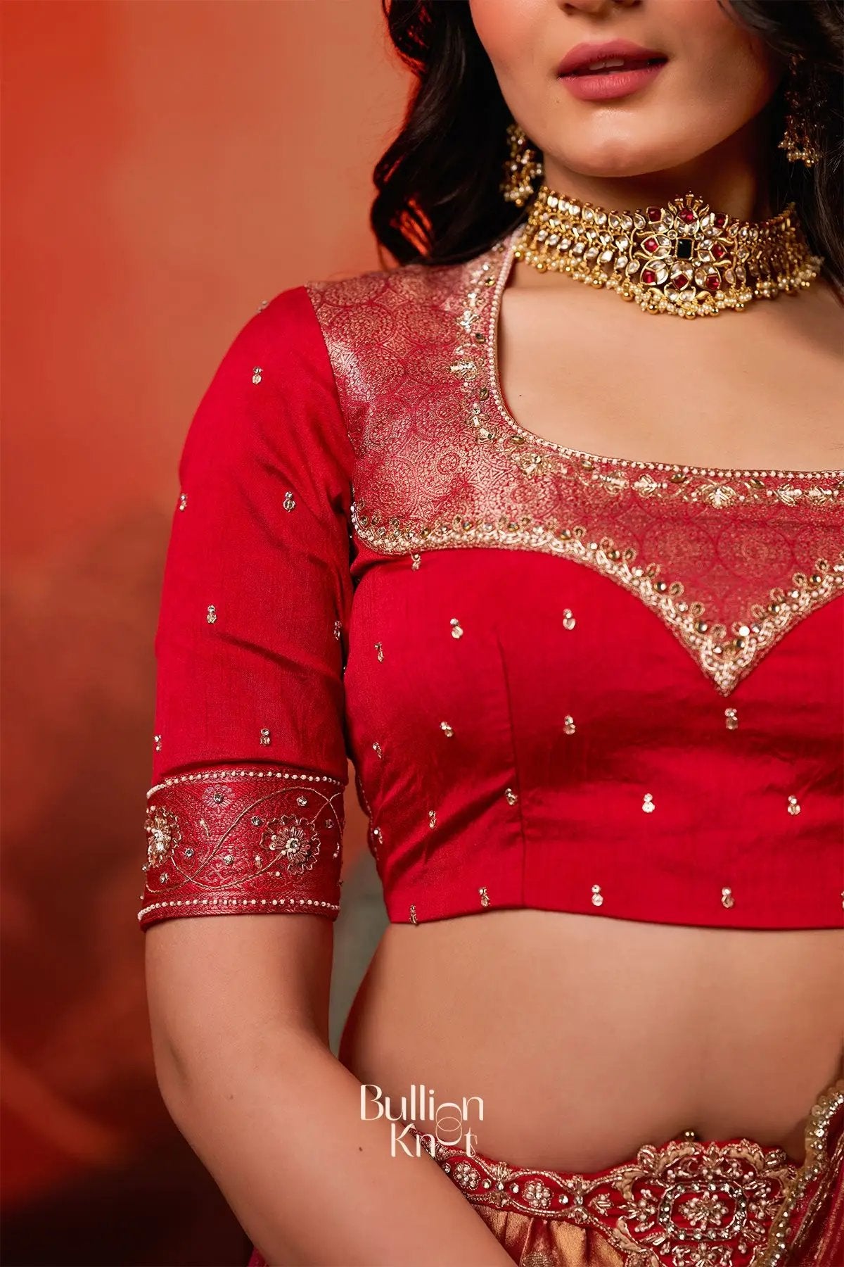 Close-up of Exclusive Lehenga - Amulya Tissue Zari Lehenga Set in Red at bullionknot showing intricate zari work on the red blouse with gold embroidery.