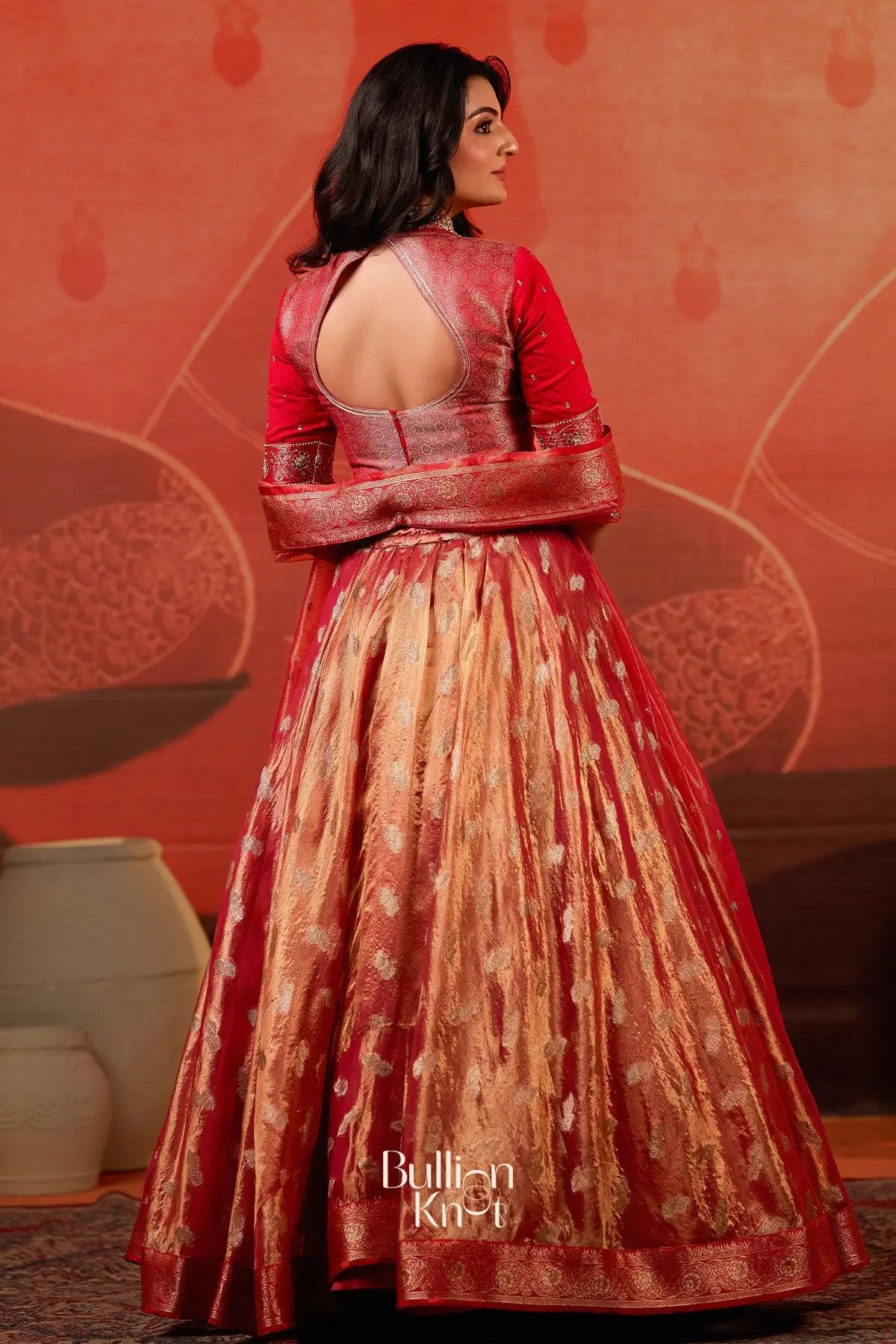Back view of Exclusive Lehenga - Amulya Tissue Zari Lehenga Set in Red at bullionknot, featuring a keyhole blouse design and flowing gold zari skirt.