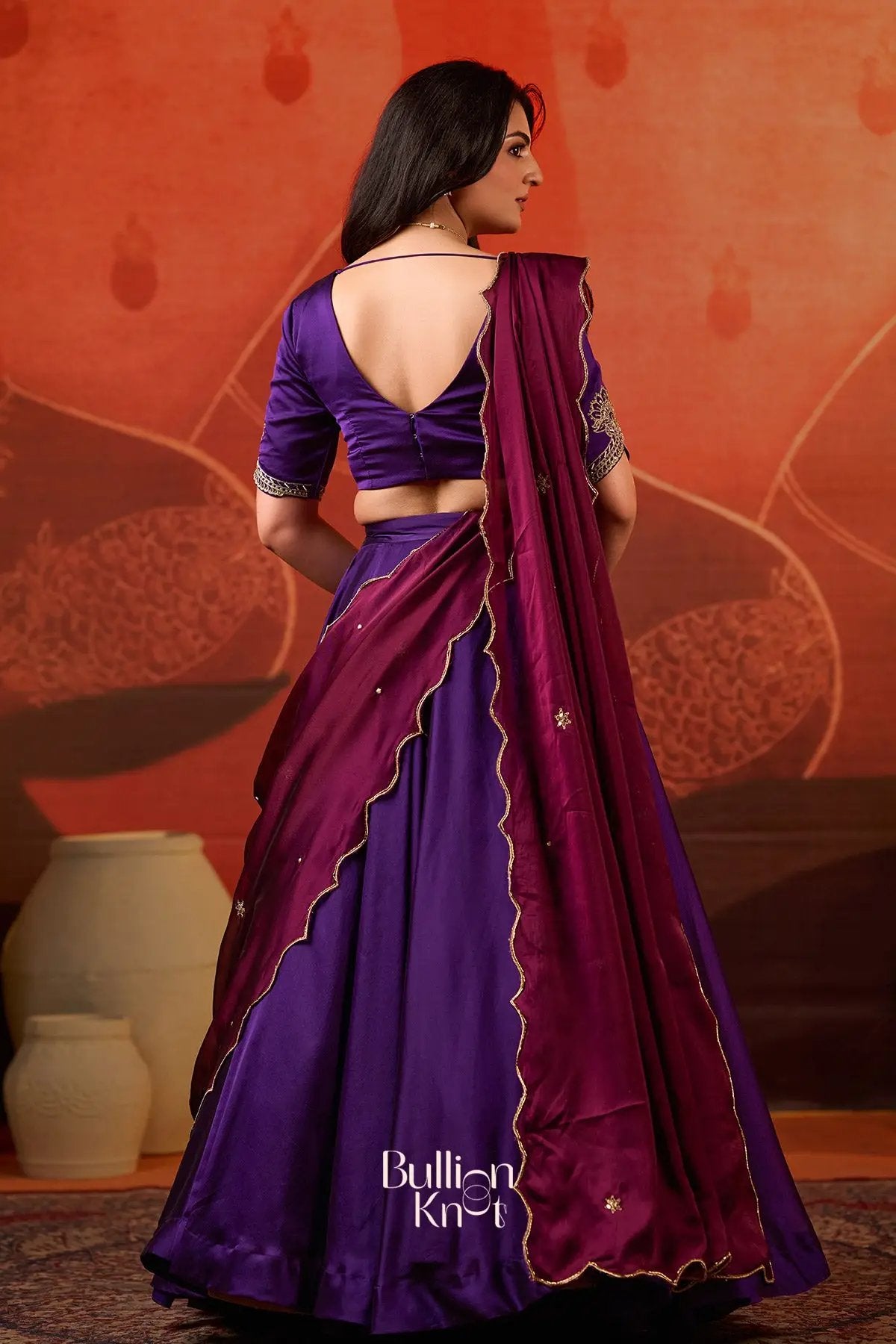 Back view of Exclusive Lehenga - Ariana Charm Lehenga Set in Purple at bullionknot, highlighting the open-back blouse and embroidered dupatta.