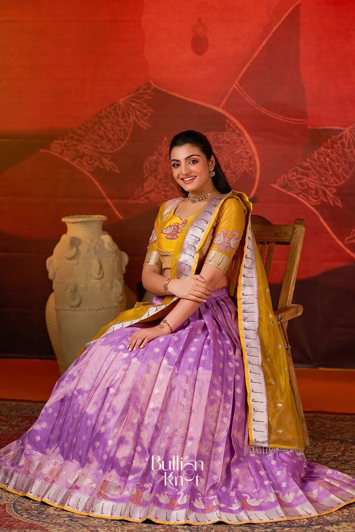 Seated model in Kumudini Kota Lehenga Set in Lavender at bullionknot showcasing pleated lavender skirt and mustard yellow blouse with embroidery.