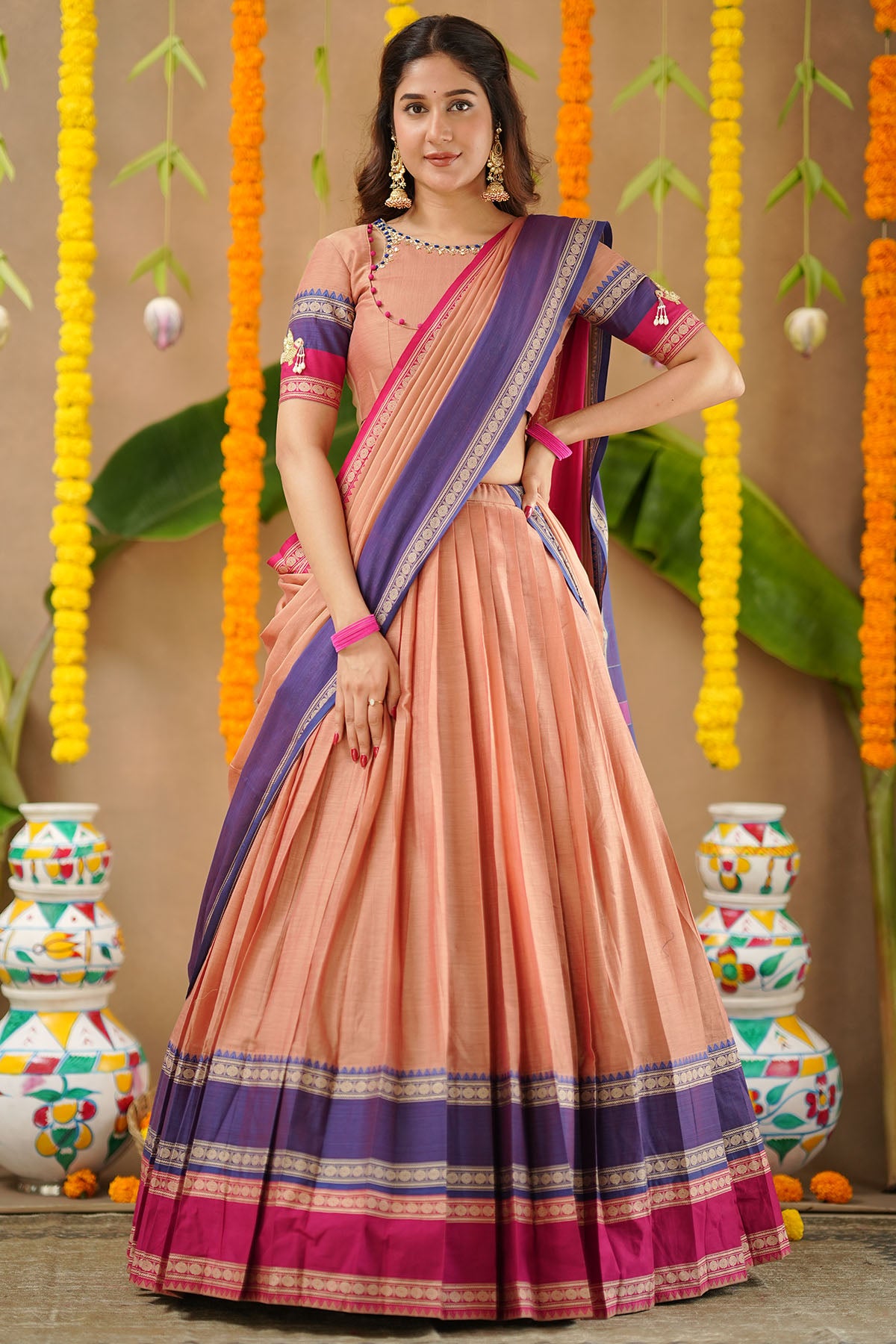 Woman wearing a peach and purple saree with decorative background