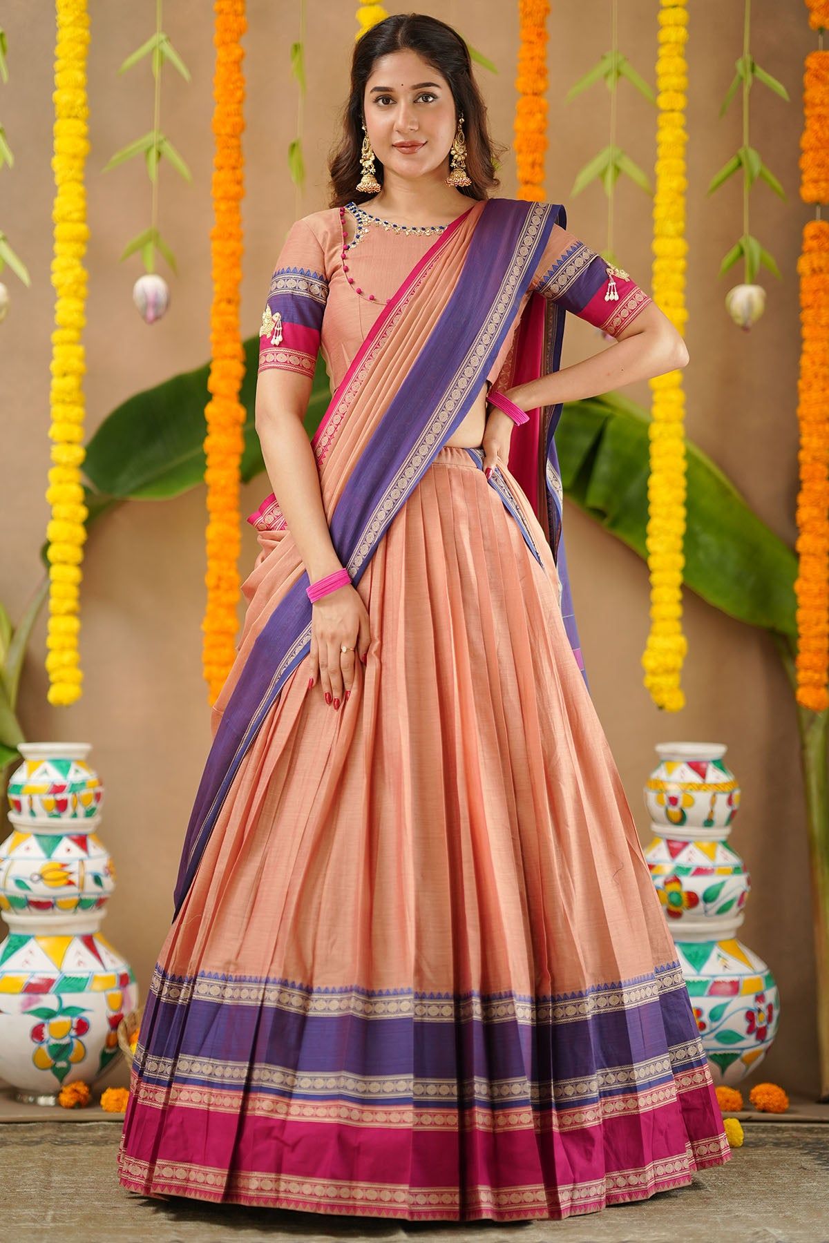 Woman wearing a peach and purple saree with decorative background