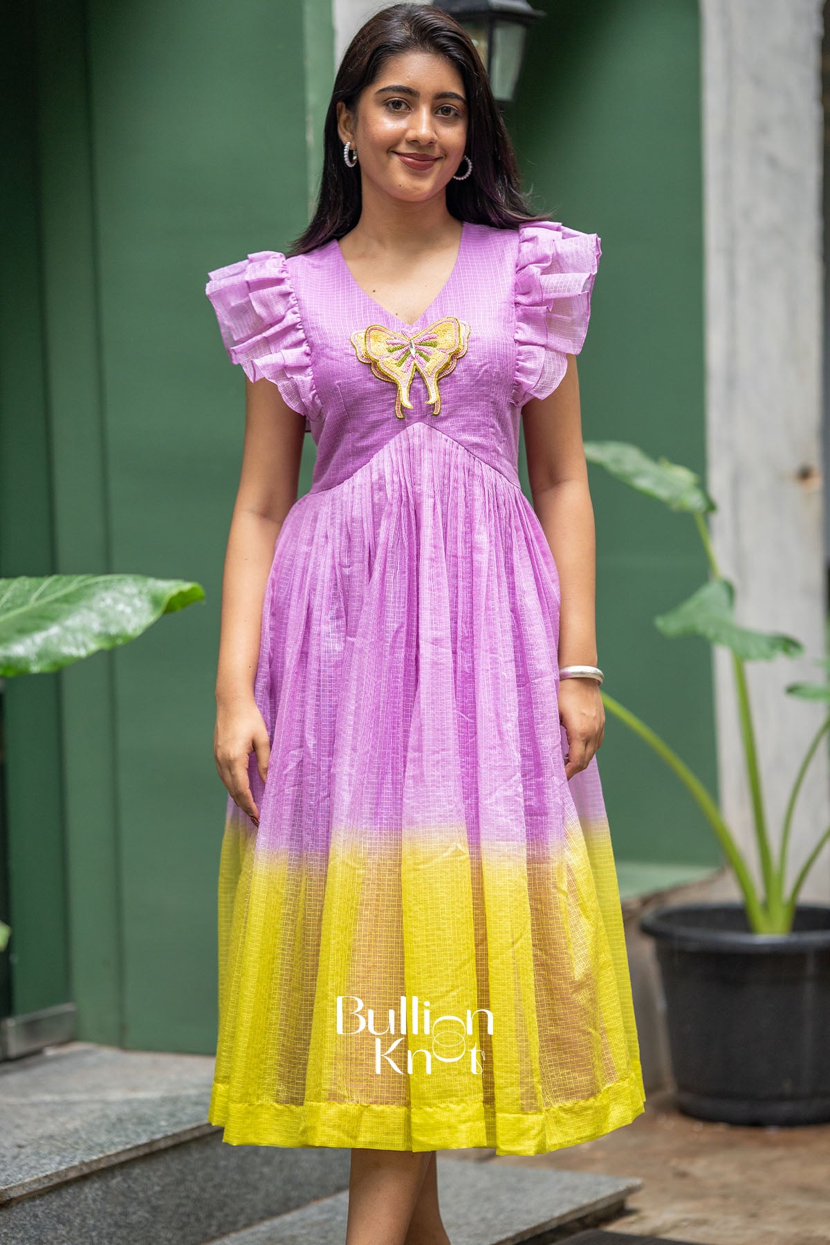 Woman wearing a purple and yellow dress with ruffled sleeves, standing outdoors.