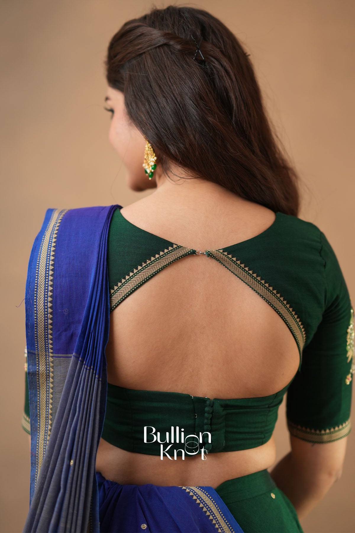 Woman wearing a green and blue saree with a visible brand logo on a beige background