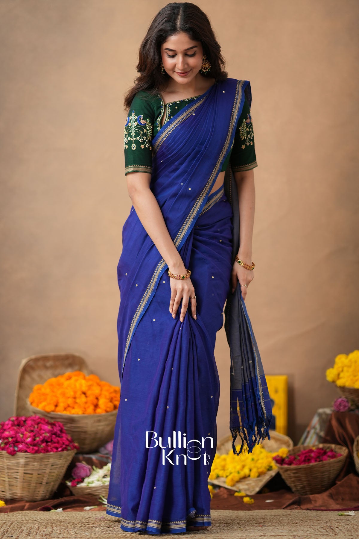 Woman wearing a blue saree with green blouse against a beige background