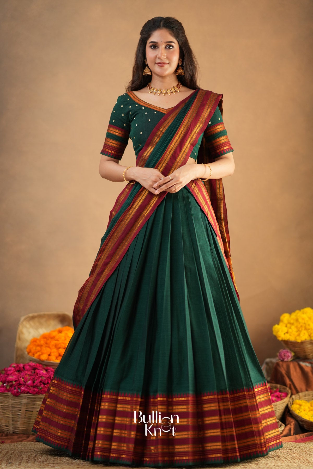 Woman wearing a green and red saree with a neutral background