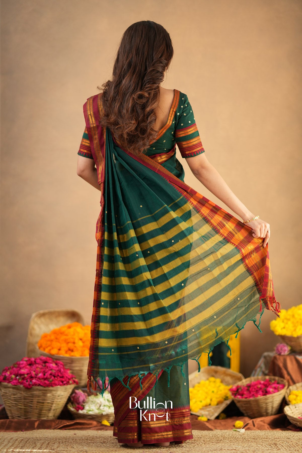 Woman wearing a green and orange striped saree with a neutral background