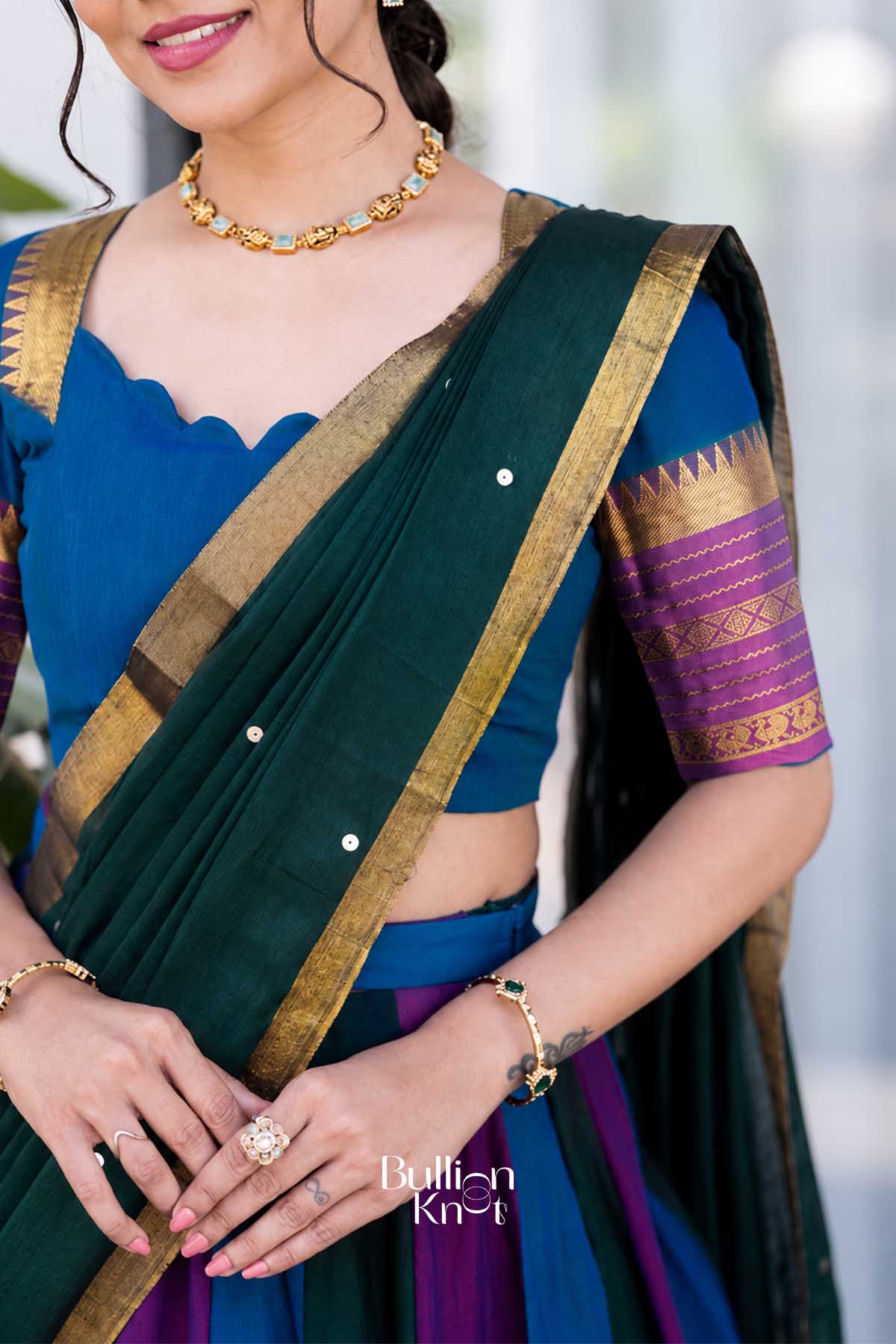 Close-up of woman’s face with pink lipstick, gold jewelry, and blue blouse with purple and gold embroidered sleeves, showcasing traditional attire.