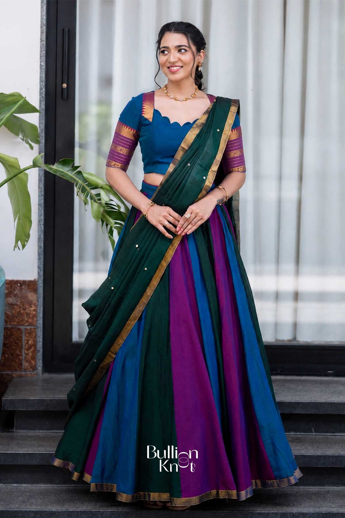 Front view of woman wearing vibrant multicolor handloom half saree with gold border, paired with gold jewelry, smiling indoors