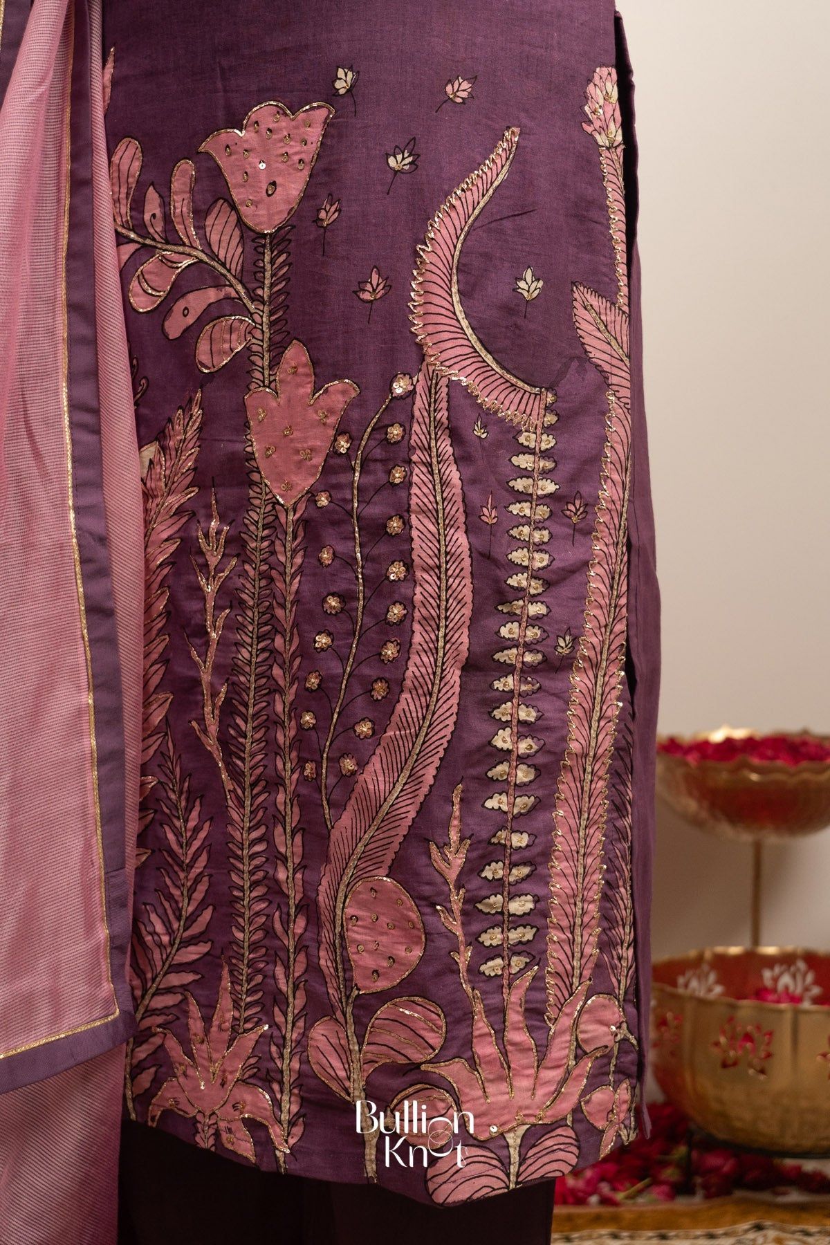 Model in purple Kalamkari dress with floral and leaf motifs, gold accents, and pink dupatta