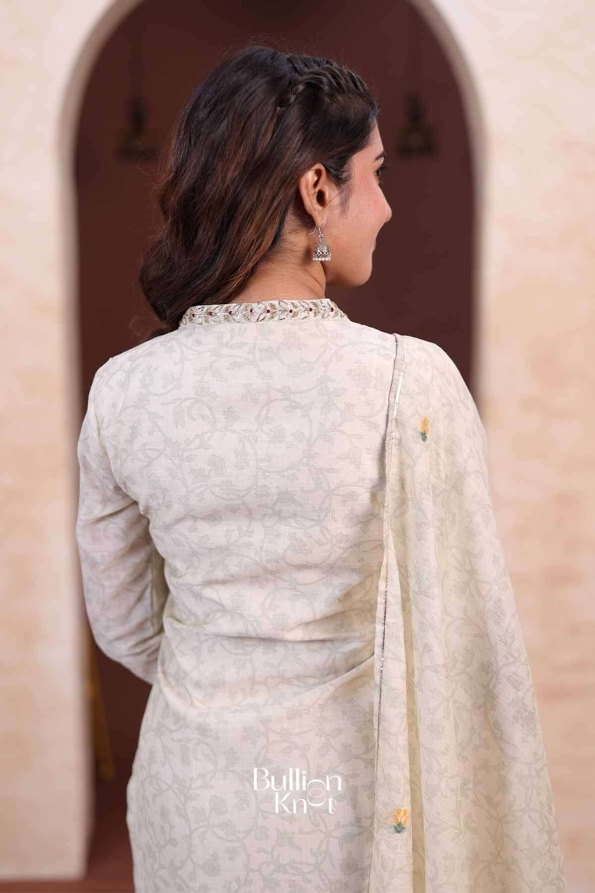 Back view of woman wearing ivory floral embroidered suit with dupatta draped over shoulder, styled with earrings