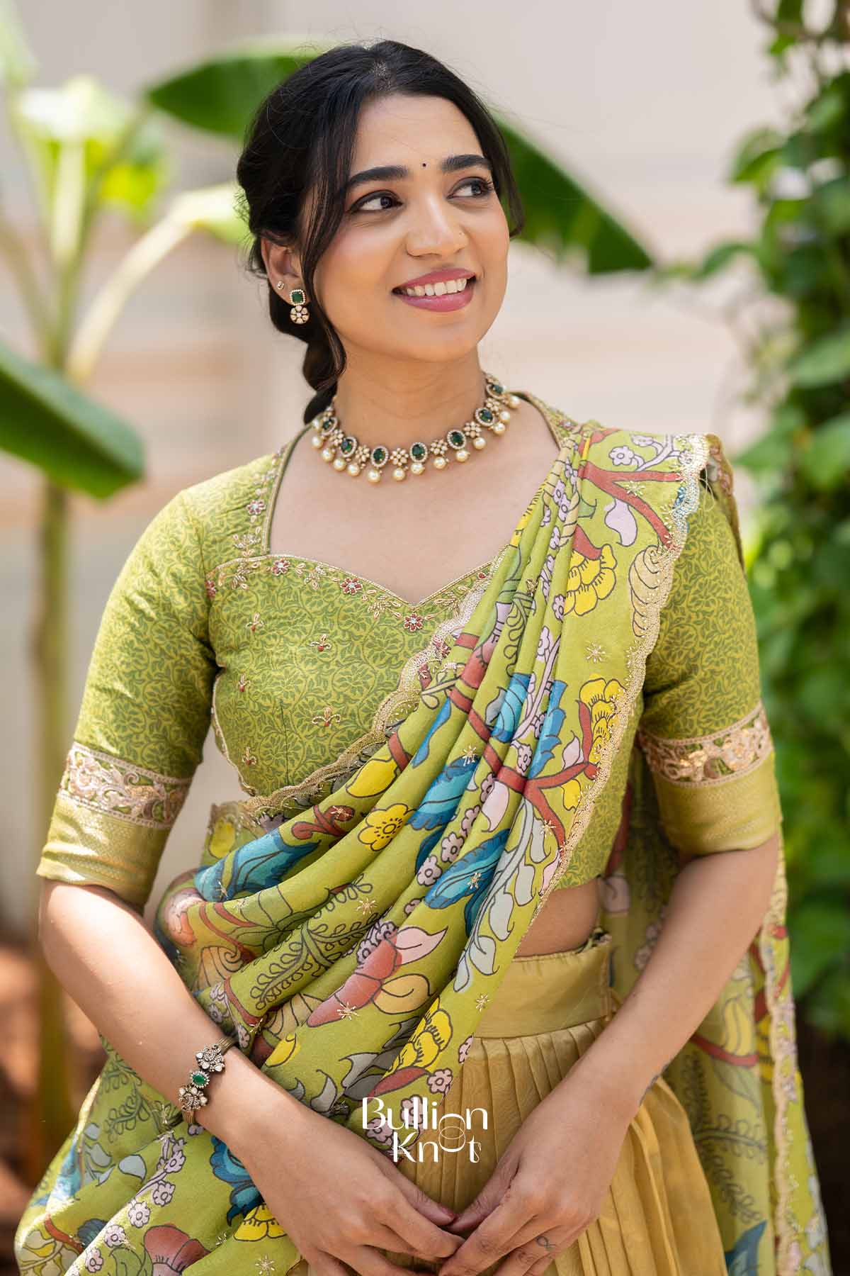 Close-up of woman wearing green embroidered blouse with floral design, matching jewelry, and colorful dupatta, showcasing traditional Indian attire.