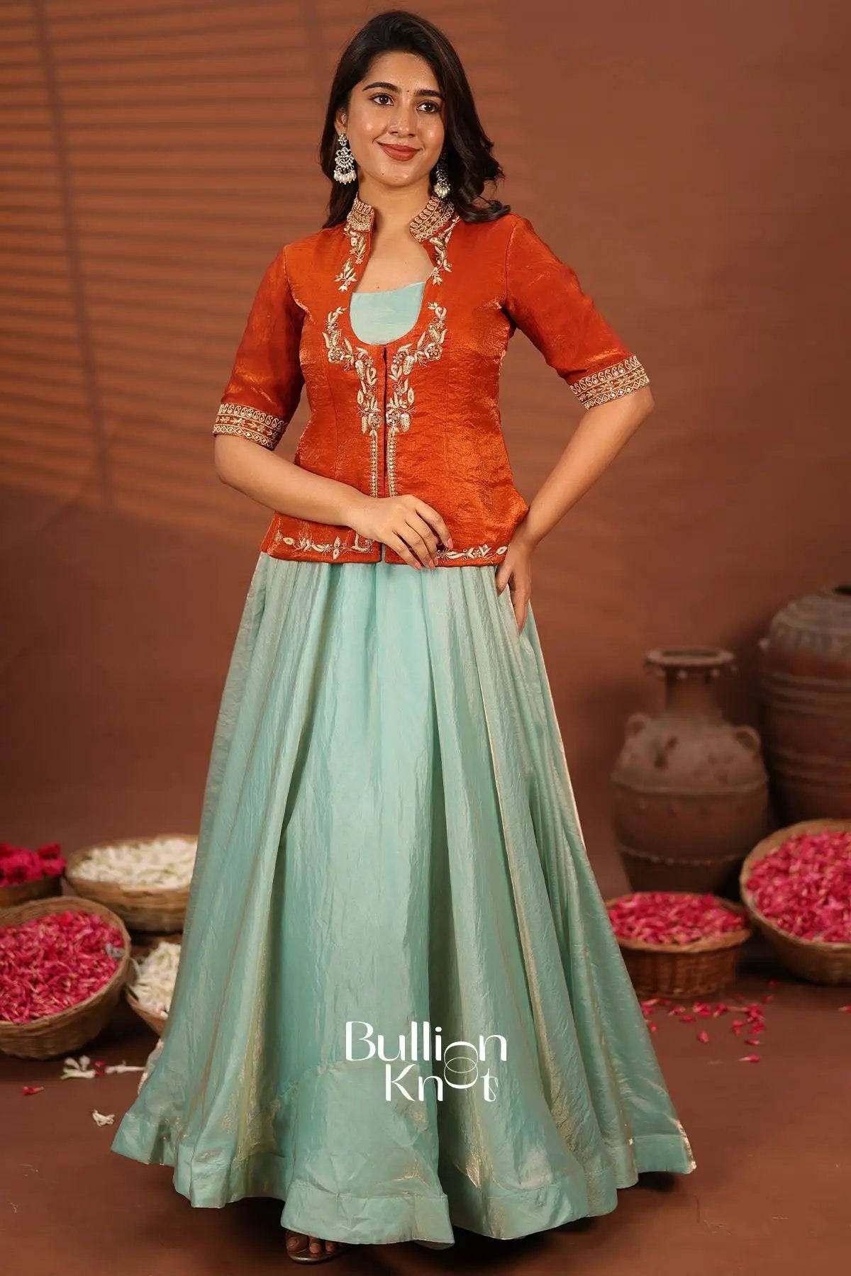 Model showcasing orange embroidered Indowestern jacket with pastel green skirt, traditional Indian attire