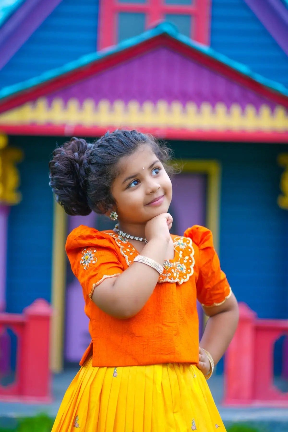 Child wearing orange lehenga set, smiling thoughtfully