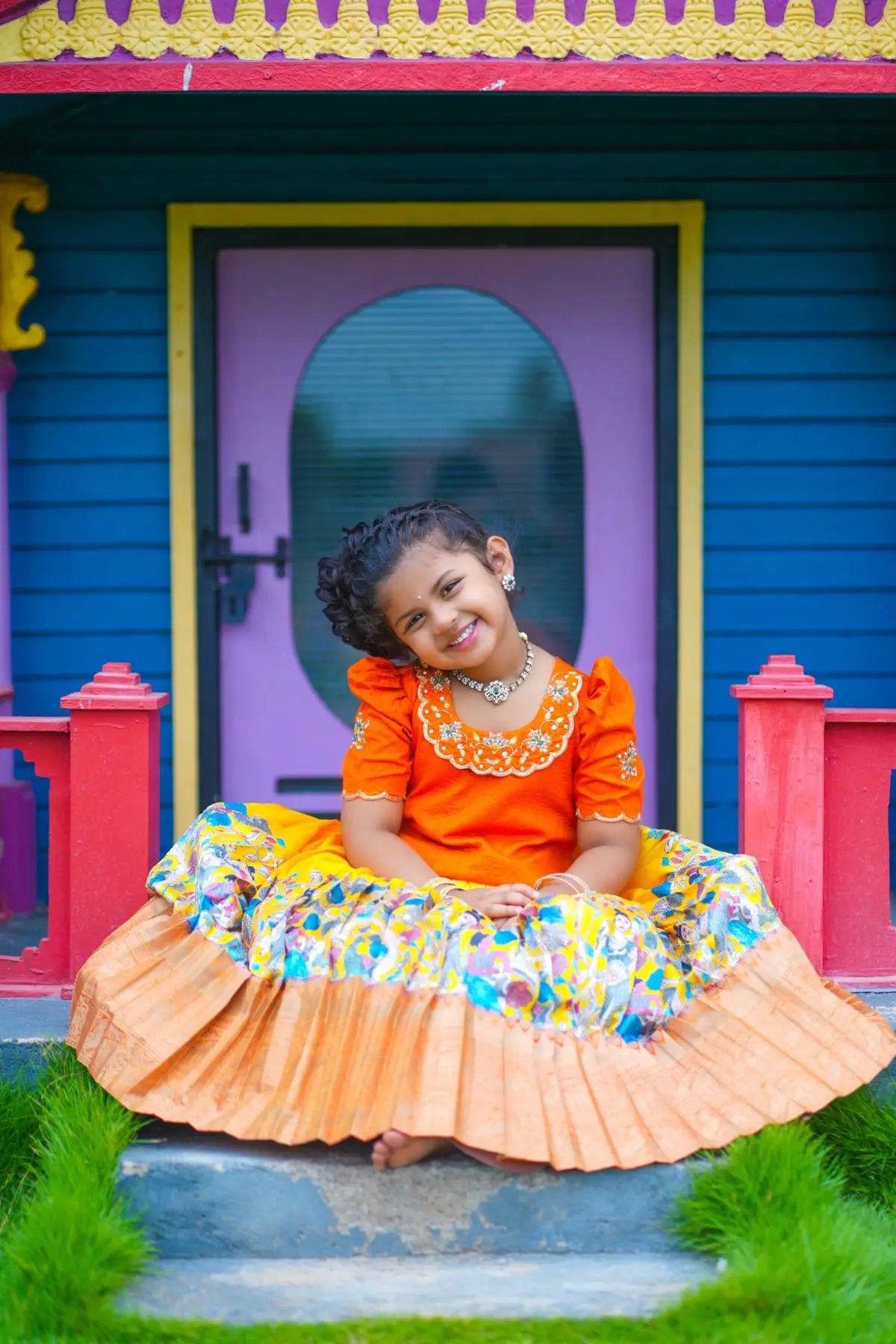 Child sitting in orange Baby Swathi Lehenga Set, smiling