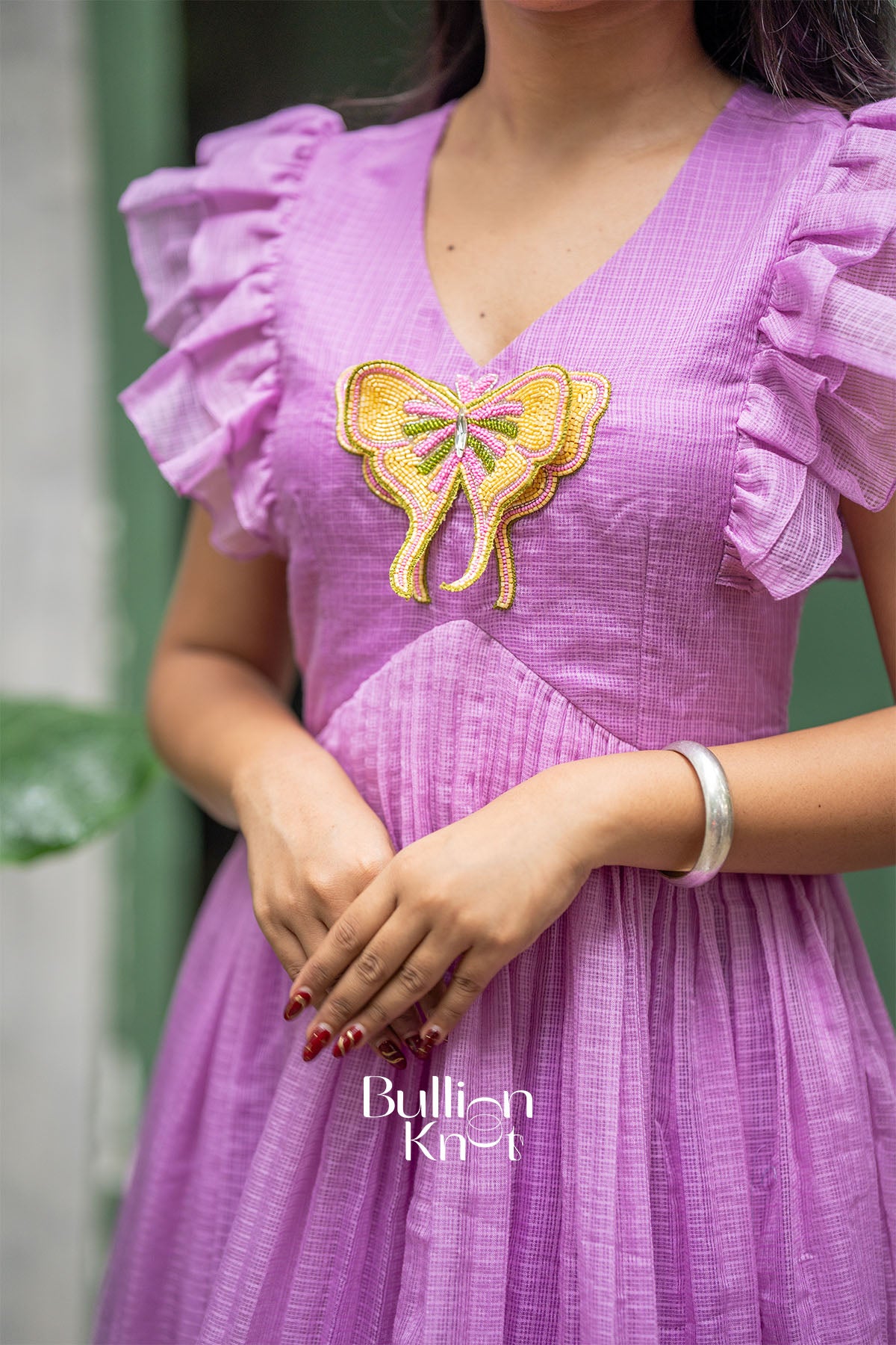 Person wearing a purple dress with a yellow embroidered bow design, standing against a green background.