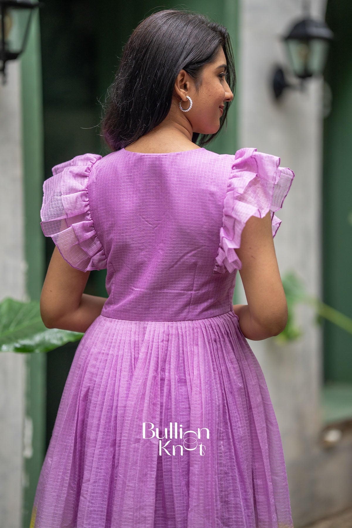 Woman wearing a purple dress with ruffled sleeves in an outdoor setting