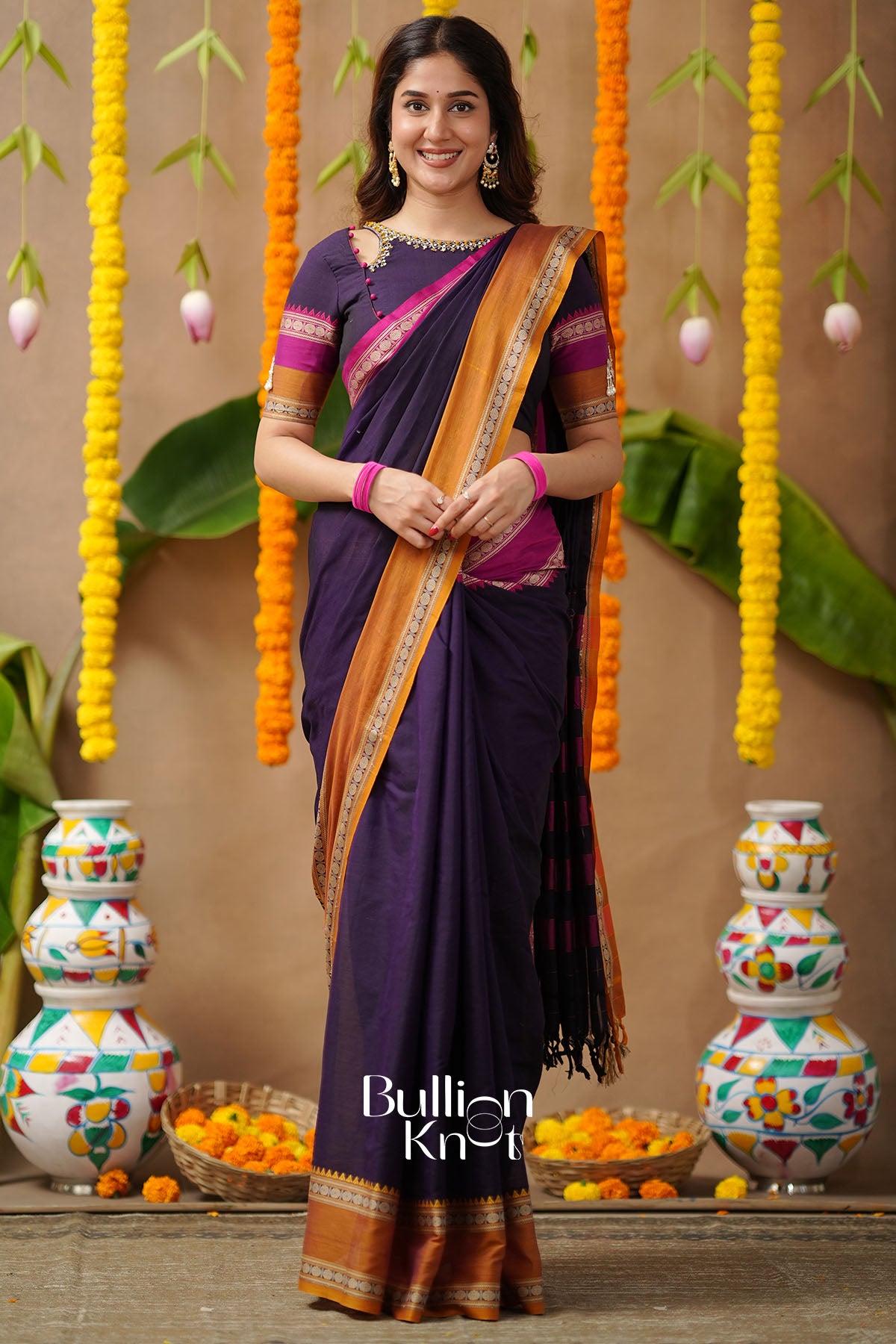 Woman in a traditional saree with decorative background and vases.
