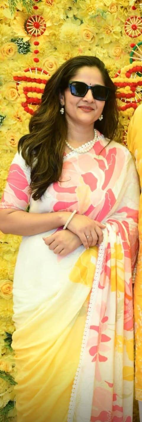 Woman in a yellow and pink saree with sunglasses against a colorful floral 