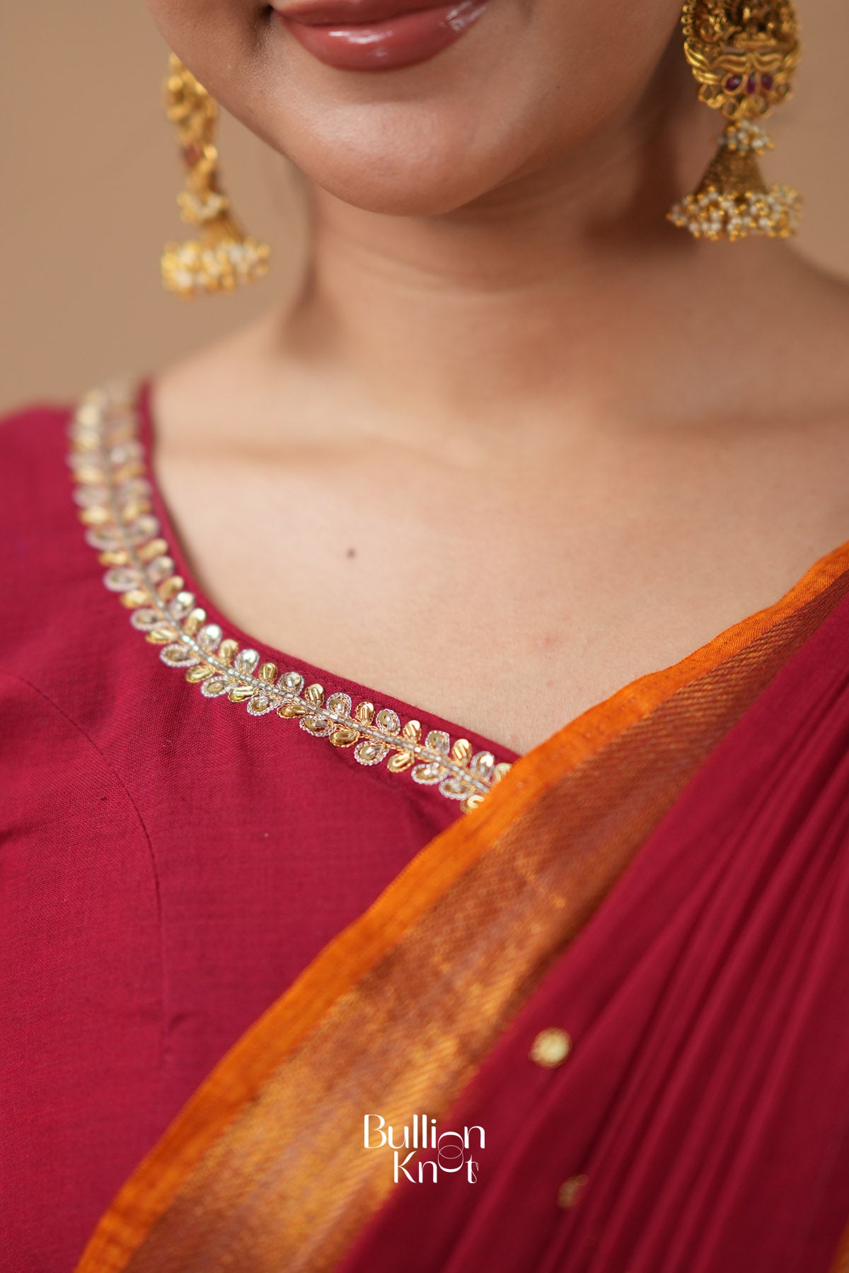 Close-up of a person wearing gold jewelry with a maroon saree 