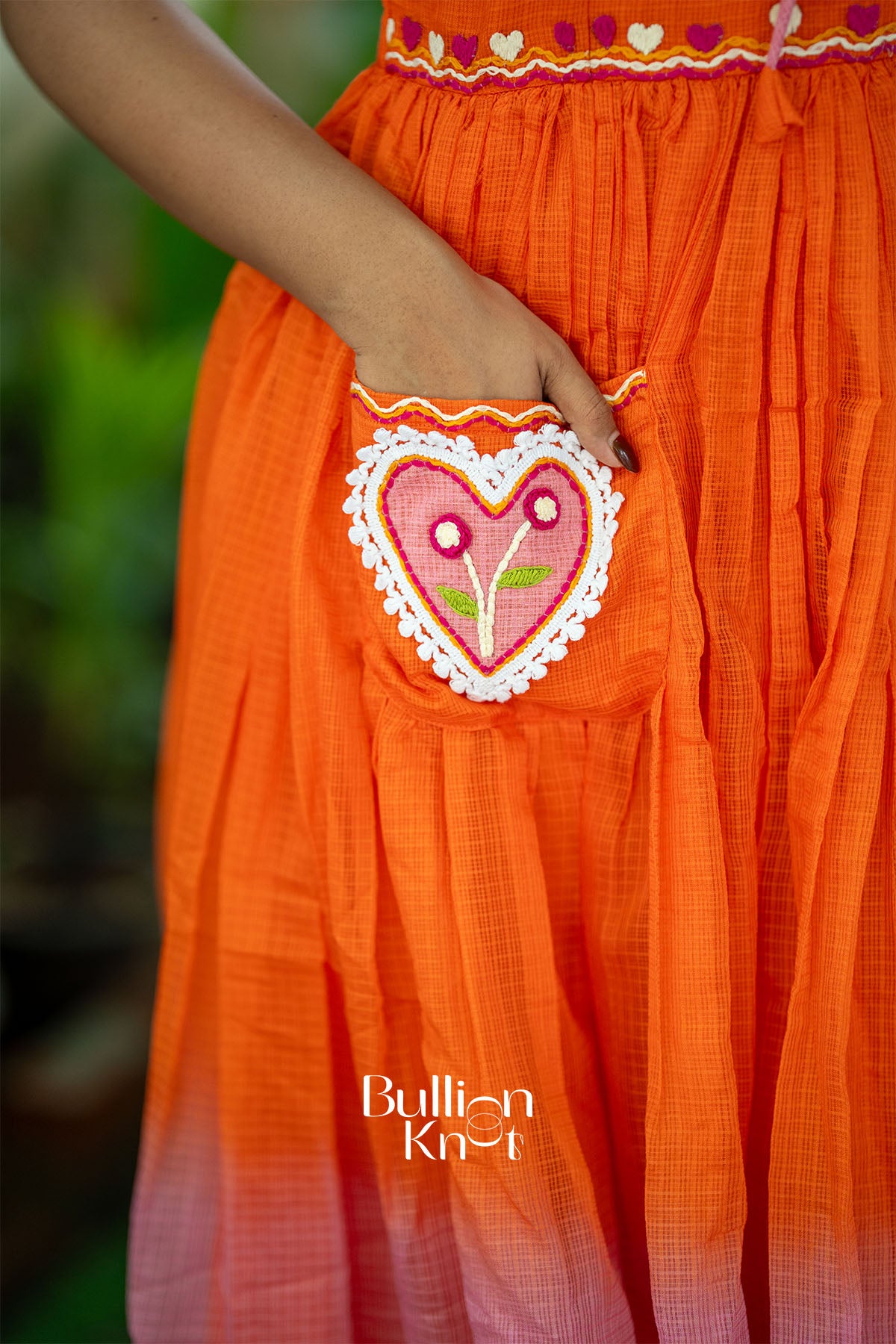 Orange dress with a heart-shaped pocket design, featuring the brand 'Bullion Knot'.
